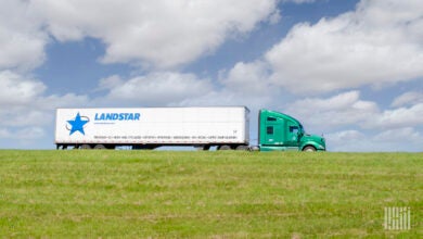 A green tractor pulling a white Landstar trailer