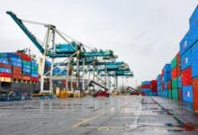 Image shows wet pavement, containers, and container cranes.
