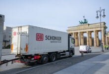 Image shows a Schenker truck and Berlin's Brandenburg Gate.
