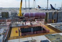 Construction work on a warehouse at the airport, with planes in the background.