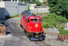 Image shows a locomotive, railroad track, trees and buildings